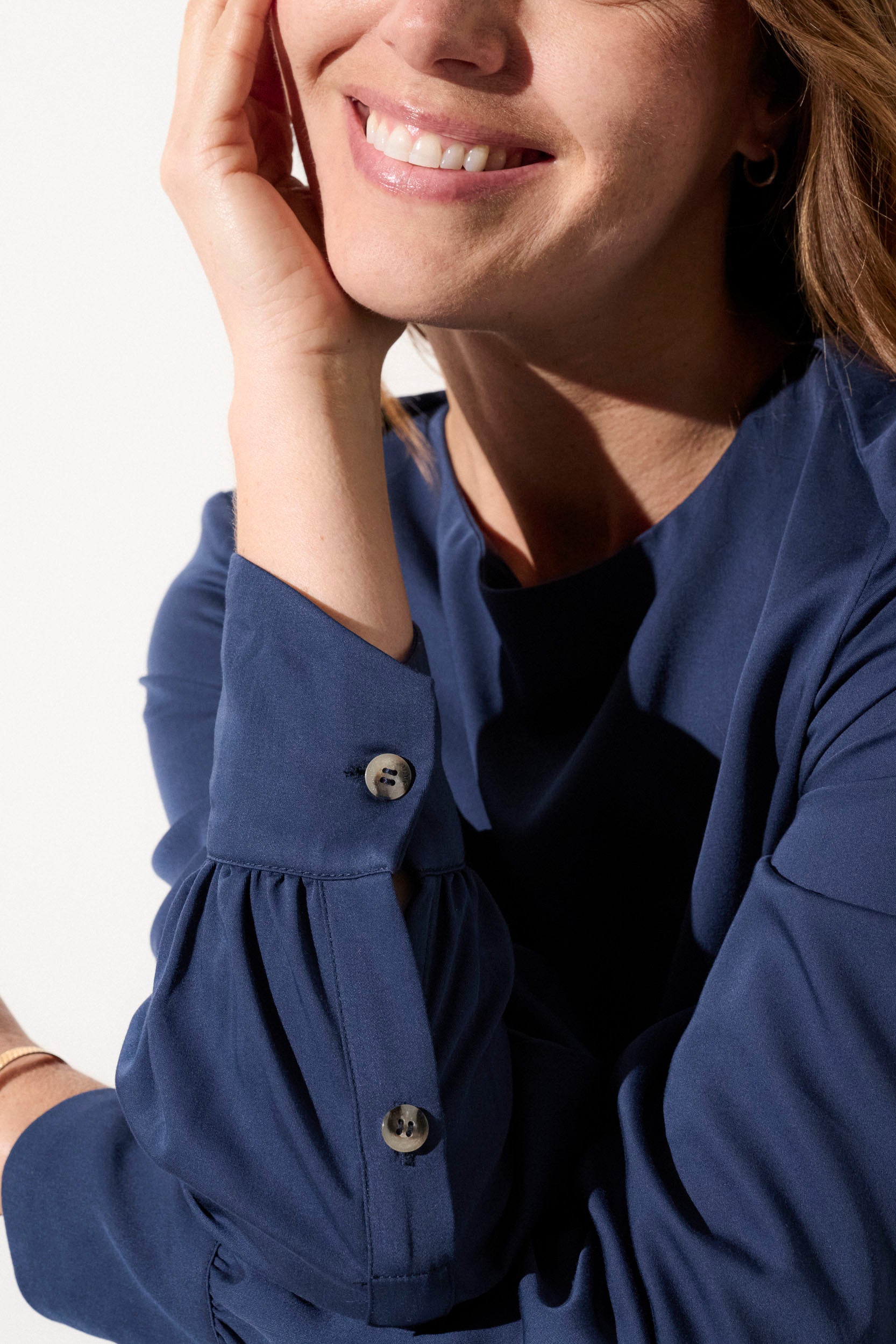 Femme souriante en blouse bleue, élégante et légère, offrant protection anti-UV UPF50+, idéale pour sorties ensoleillées.