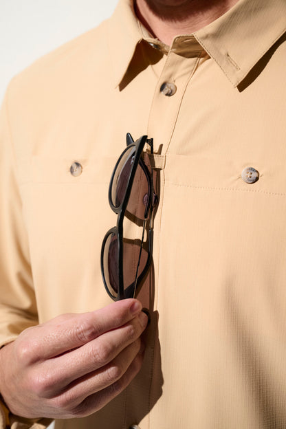 Homme portant une chemise légère beige anti-UV tout en tenant des lunettes, idéal pour les activités en extérieur.