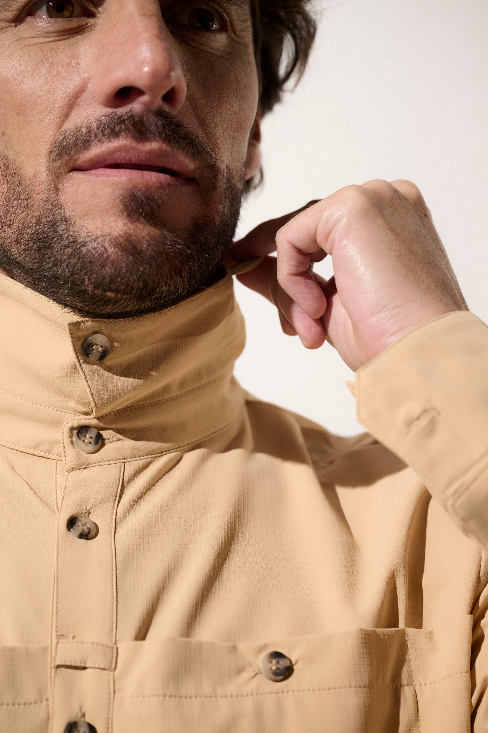 Homme ajustant le col d'une chemise anti-UV beige UPF50+, idéale pour la protection solaire en plein air.