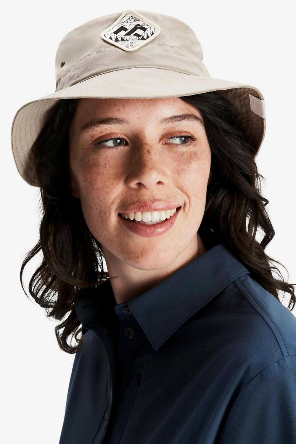 Femme souriante portant un chapeau anti-UV beige, parfait pour la protection solaire en plein air.