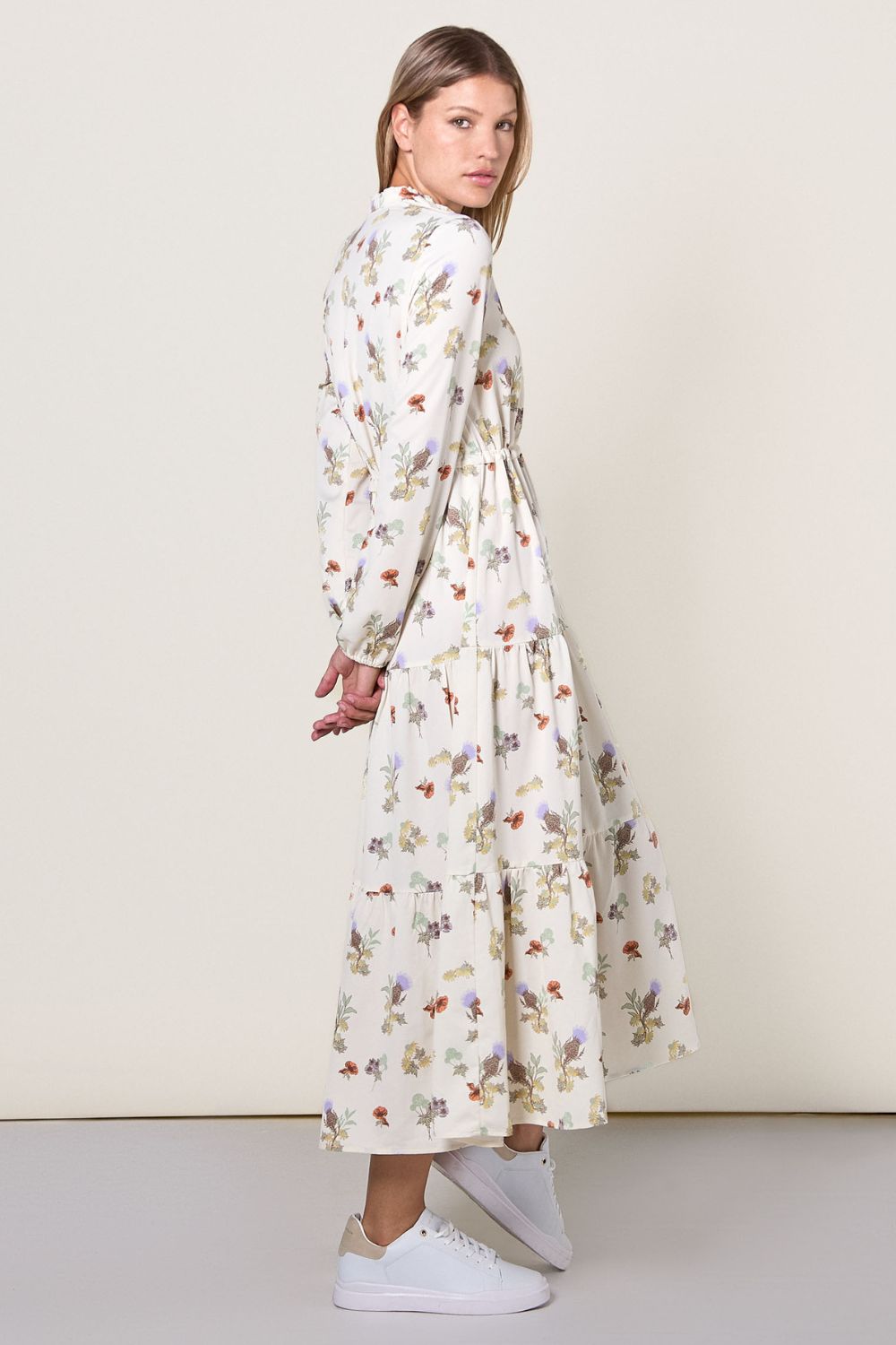 Robe longue anti-UV à manches longues pour femme, motif floral élégant et protection UPF 50+, portée avec des baskets blanches.