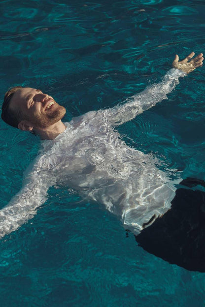 Homme flottant dans une piscine, portant un t-shirt de bain anti-UV blanc UPF 50+ pour une protection solaire optimale.